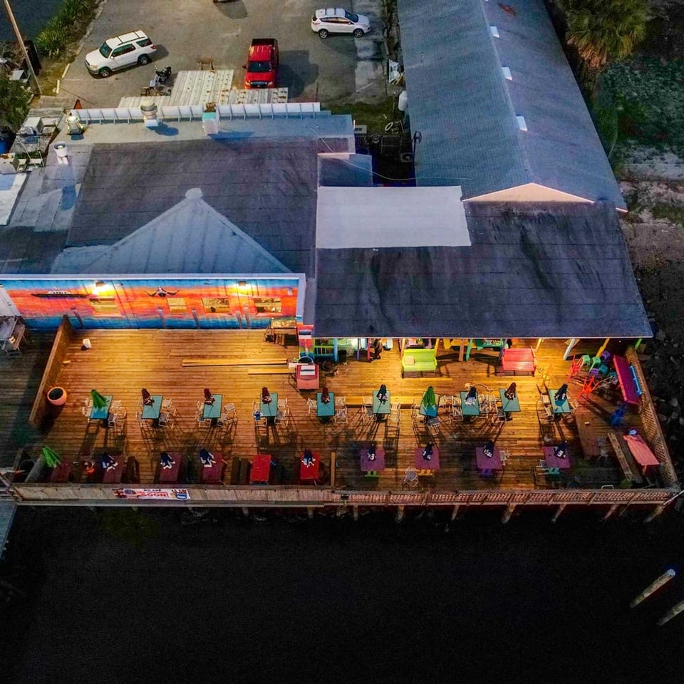 Aerial view of a restaurant with a brightly lit outdoor deck over dark water at night.