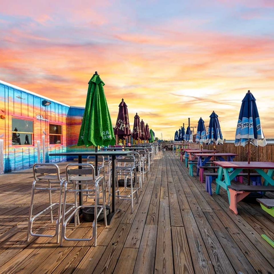 Colorful restaurant building and outdoor seating on a wooden deck at sunset.