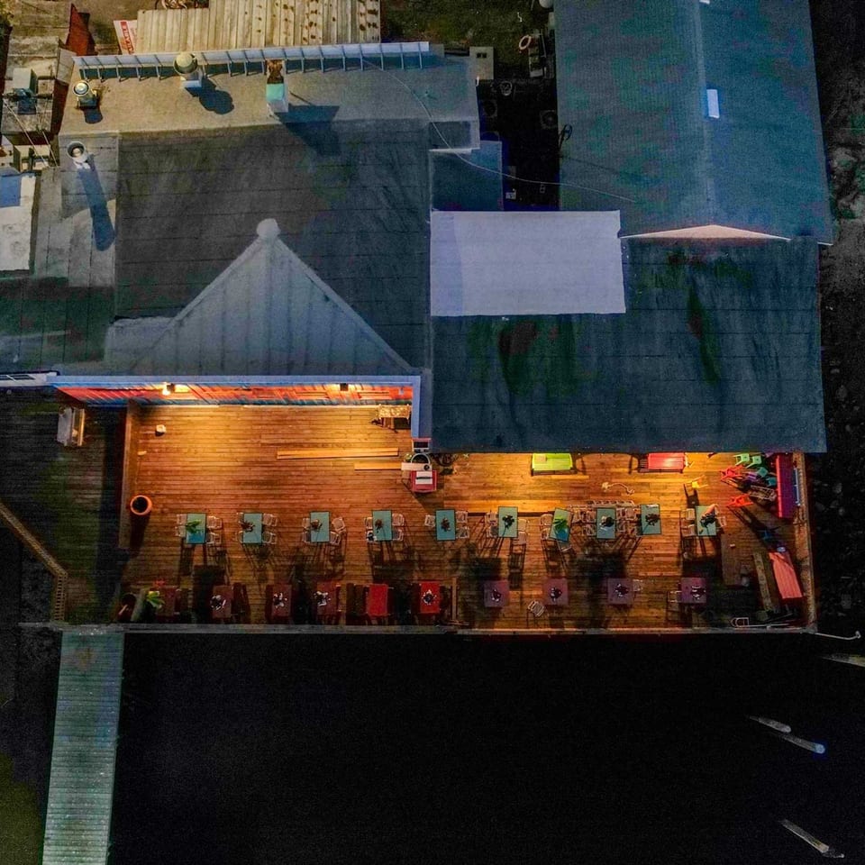Aerial view of a restaurant with an illuminated outdoor patio deck over dark water at night.