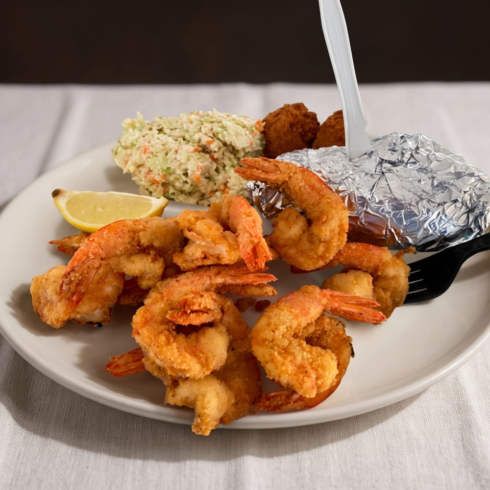 Fried shrimp platter with coleslaw, hush puppies, a baked potato, and lemon wedge.
