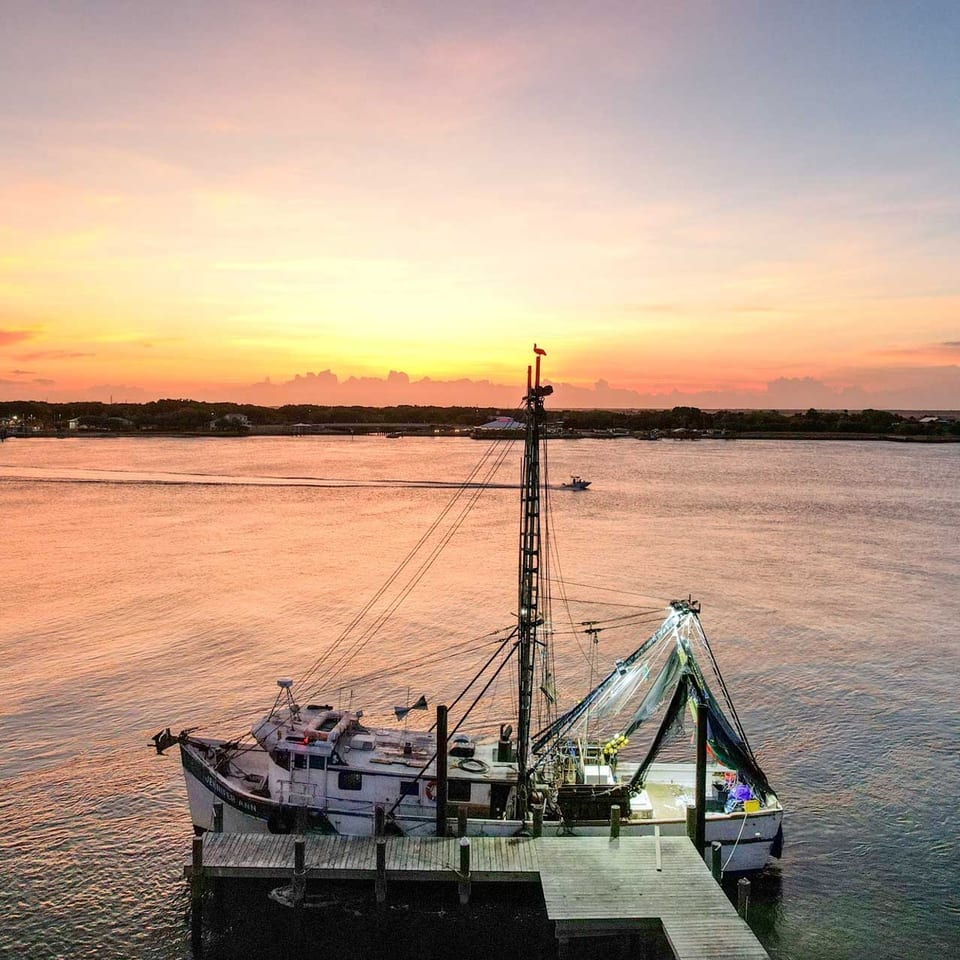 A fishing boat docked at sunset, with a vibrant orange and pink sky over the water.