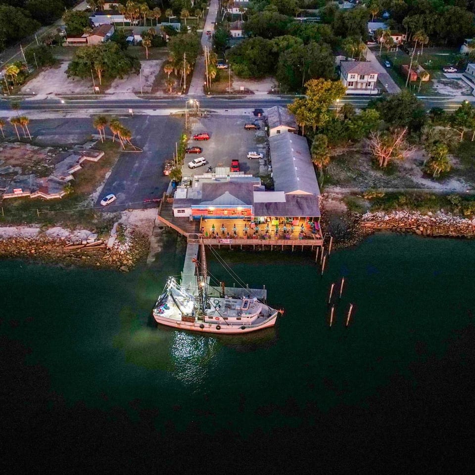 Aerial view of a waterfront restaurant with a boat docked at its pier at dusk.